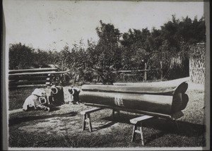 A closed chinese coffin made of four half trees and painted red. The (female) relatives lying in front of the coffin lead the lamentations