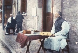 A man working as a combination letter-writer and fortune-teller and a man working as a barber in the same street, Shanghai, Shanghai Shi, China, ca.1900-1919