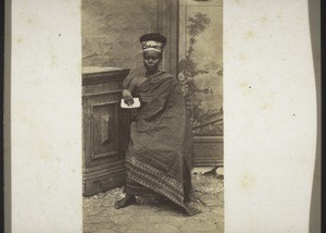 Ga woman with head-tie and her hair-style showing above it, rings on her fingers, ears and toes etc