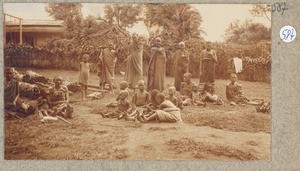 Chagga on grassland in front of a hedge-fence and a European house, Tanzania, ca.1900-1914