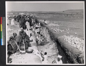 People gathering on an arid plain by a deep trench, India, ca.1919-1943