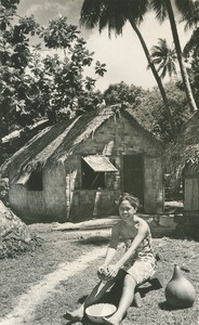 Tetua grates coconut, in front of her hut