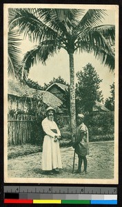 Missionary father standing with man beneath a palm tree, Madagascar, ca.1920-1940