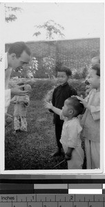 Man holding a small ball out to young orphans, Loting, China, ca. 1935