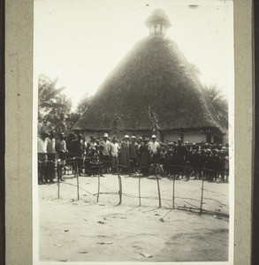 Empfang vor der Kirche i. Bengwi b. Bamendig. Links sitzt der Häuptling, rechts der Evangelist Asili. Hier wurden innerhalb von 8 Jahren 3 Kirchen gebaut, bald ist auch diese zu klein. (1928)