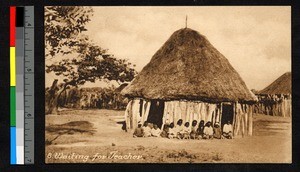 Children sitting before a round, thatch-roofed building, Angola, ca.1920-1940