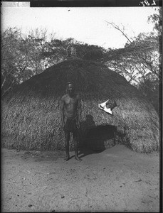 African man standing in front of a hut, Mozambique, ca. 1901-1907