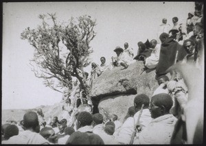 Court scene at an annual fair. The judge is sitting on the rock, in a hat