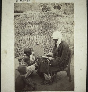 Haussa teacher with students. In the background a plaited grass mat as wall