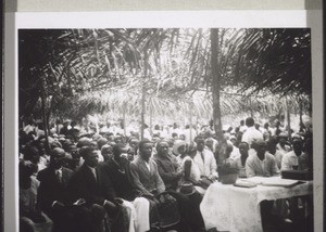 A so-called mission festival in Victoria: a meeting of all the christian congregations of the area around the station in Victoria. The festive meeting-house is a roof of Palm leaves