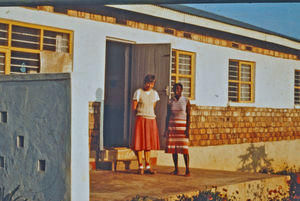 Lægemissionær i DMS Karen Borgbjerg med hushjælp foran huset, som hun deler med cand. theol. Ida Kongsbak. Foto december 1986. (Karen Borgbjerg var udsendt til Nyakahanga Hospital, 1985-89. Ida Kongsbak til undervisning af lægfolk i Karagwe stift, 1985-95)