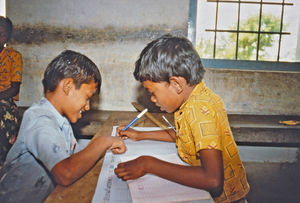 33.- Tamil Nadu, Indien, 1988-89. "Med 80 elever i klassen" - En dansk lærer i Arcot skoleprojekt fortæller: Hjemme på skolen blev alle oplysninger sorteret og behandlet. Her er drengene i gang med at nedskrive alle landsbyens helligdage, både nationale og lokale, for hinduer, muslimer og kristne. Det kunne hurtigt blive forvirrende, så de fandt ud af at bruge en farve for hver religion for at holde orden på det