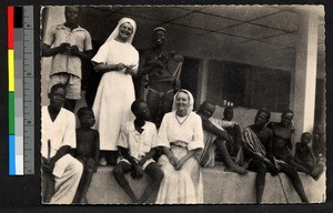 Two missionary sisters gather with people on a verandah, Cameroon, ca.1920-1940