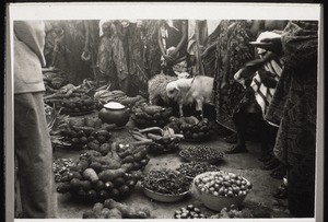 Geschenke des Begorokönigs zur Synode: Versch. Früchte: Yams, Erdnüsse, Tomaten etc; i. d. Mitte ein Topf mit Wasser. Der Träger rechts hält i. der Hand 1 weissen Teller mit Geld, das mit weisser Wolle zugedeckt ist