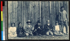 Missionary father and other people seated outside of a wooden building with some holding pipes, Canada, ca.1920-1940