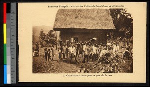 People working in a field before a thatch-roofed building, Cameroon, ca.1920-1940