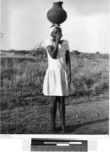 Girl on a dirt road balancing a pot on her head, Africa, July 1949