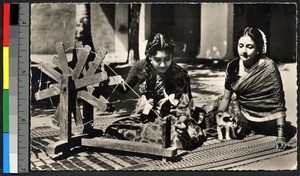 Two young women working a spinning wheel, India, ca.1920-1940