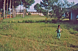 Nordveststiftet, Tanzania, 1984. Billedet viser en del af Ntoma Husholdningsskole. Den blev bygget i 1969, og da missionær Gudrun Larsen arbejdede der (1974-86), var der fem lærere. Lederen var Judes Kamala, som havde ledet skolen siden 1974. Derudover var der en skolekok og en til at tage sig af det praktiske med eleverne uden for selve undervisningen. Barnet i forgrunden er Gudrun Larsens 'barnebarn' Upendo