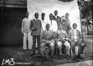 Group of men sitting and standing in rows in front of the mission house, Antioka, Mozambique, ca. 1901-1915