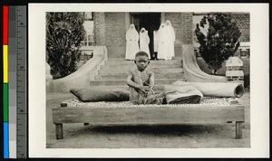 Child sitting on a bed outdoors, Congo, ca.1920-1940