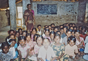 07.- Tamil Nadu, Indien, 1988-89. "Med 80 elever i klassen" - En dansk lærer i Arcot skoleprojekt fortæller: Sådan ser der ud indenfor i de gamle skoler. Det eneste hjælpemiddel, man har, er faktisk tavlen i baggrunden. Derfor er undervisningen næsten altid mundtlig. Det giver selvfølgelig en masse larm, så børnene her glæder sig til at få nogle flere lokaler. De får nok ikke et lokale til hver klasse, men sikkert 2-3 lokaler. Og det skal de nok finde ud af at klare sig med