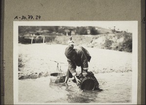 A woman washes her basket in the river