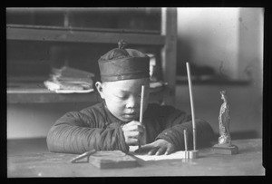 Boy seated at a table writing, China, ca. 1918-1938