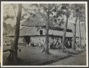 People sitting in front of house with two-tiered roof, Tanzania