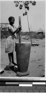 Girl using a large pestle to grind food, Africa, October 1947