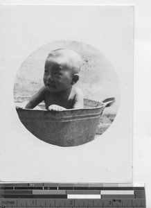 A baby sitting in a wash basin at Ducheng, China, 1935