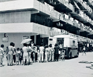 Kwun Tong Vocational Training Centre i Hongkong blev grundlagt i 1965 af LWF/LWS’ regionale afdeling – på et tidspunkt hvor "byen var så fattig, at det var almindeligt for velgørende organisationer at uddele gratis mælkepulver". Centret blev gennem mange år pioner for en række erhvervsfaglige kurser, med henblik på at sikre studerende fra lavtlønnede familier et levebrød. De forskellige fag blev løbende tilpasset den aktuelle udvikling i samfundet. Et af de første kurser var et diplom-program i fotografering, som blev meget efterspurgt. Dette foto - som viser folk i kø for at få udleveret gratis mælkepulver - er taget, fremstillet og printet af studerende på centret