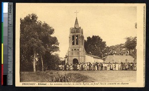 Large group in front of a church with a bell tower and a school, Athieme, Benin, ca. 1900-1930