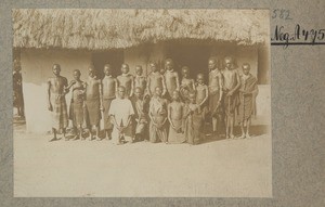 African men in front of a rectangular house with plant fiber roof, ca.1900-1914