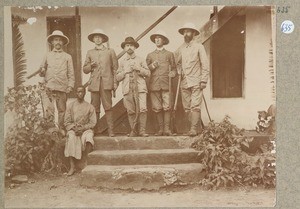 5 Europeans with guns and 1 African at the stairs to an entrance, ca.1901-1914