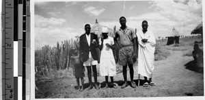 Group of people standing on a dirt road next to several huts, Africa, April 9, 1947