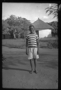 African boy standing in front of a hut, Africa, ca. 1940-1950