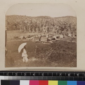 View of forest village with missionary in white suit and parasol in foreground, Madagascar, ca.1865-1885