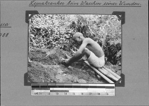 A leper washing the wounds on his feet, Isoko, Tanzania, 1929