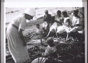 Die Mädchen der Mädchenschule Viktoria verfertigen Besen aus Palmrippen am Meeresstrand, Frln Sarasin schaut ihnen zu