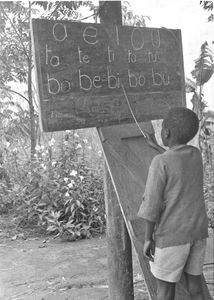 Bukoba, Tanganyika (fra 1964 Tanzania). En dreng øver sig på alfabetet i den udendørs børnehaveskole