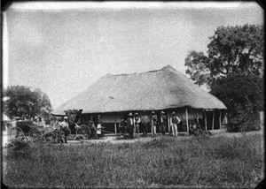 Swiss missionaries and African people in front of a building with a thatched roof, southern Africa, ca. 1880-1914