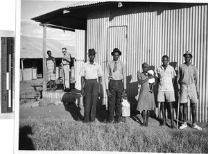 Five adults and two children standing in a row along a building, Africa, November 1950