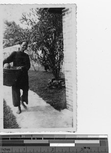 A Chinese woman carries a baby in a basket at Luoding Orphanage, China, ca.1930