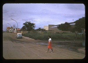 woman walking across a city street, automobile in the background