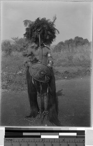 Man wearing a headdress while holding a spear and shield, Africa, ca. 1920-1940