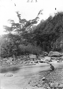 Boy squatting at the bank of a river, Tanzania, ca.1893-1920