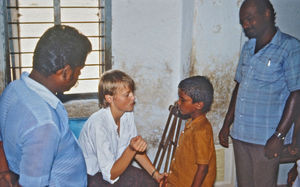 20.- Mission for børn i Indien. Diasserie 1990, "Da jeg blev velsignet af en elefant". Der var mange sygdomme, og her undersøger sygeplejerske Anne Marie Lauritsen en dreng, der er lige ved at blive blind – og det er kun pga. vitaminmangel. Kunne han få de vitaminpiller, vi spiser herhjemme, var han ikke blevet blind. Bagerst kan I se nogen krykker, fordi en dreng i klassen har børnelammelse, så han ikke kan gå