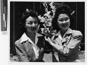 Two women holding paper flowers at the Japanese Relocation Camp, Manzanar, California, July 1942