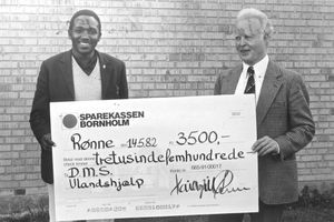 DMS landsmøde i Rønne 1982. Forud for landsmødet havde byens kirkelige ungdomsorganisationer lavet loppemarked til fordel for DMS. Det kom der en stor check ud af, som her præsenteres af pastor Samson Amos, Tanzania og økonomichef Preben Larsen